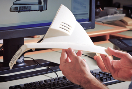 a white 3d printed part being examined next to a computer monitor