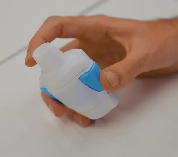 Close-up of a hand holding a small medical device prototype with white housing and blue grip features, showing its refined production-ready design.