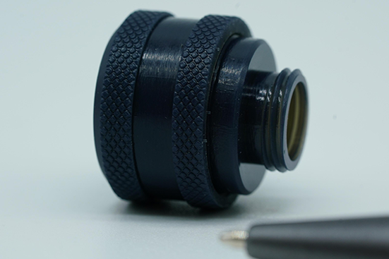Close-up of a black 3D printed threaded part with textured grip, next to pen tip for scale