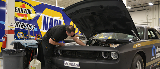 Automotive engineer performing under-the-hood testing on a Dodge Challenger prototype in a Auto Parts workshop.